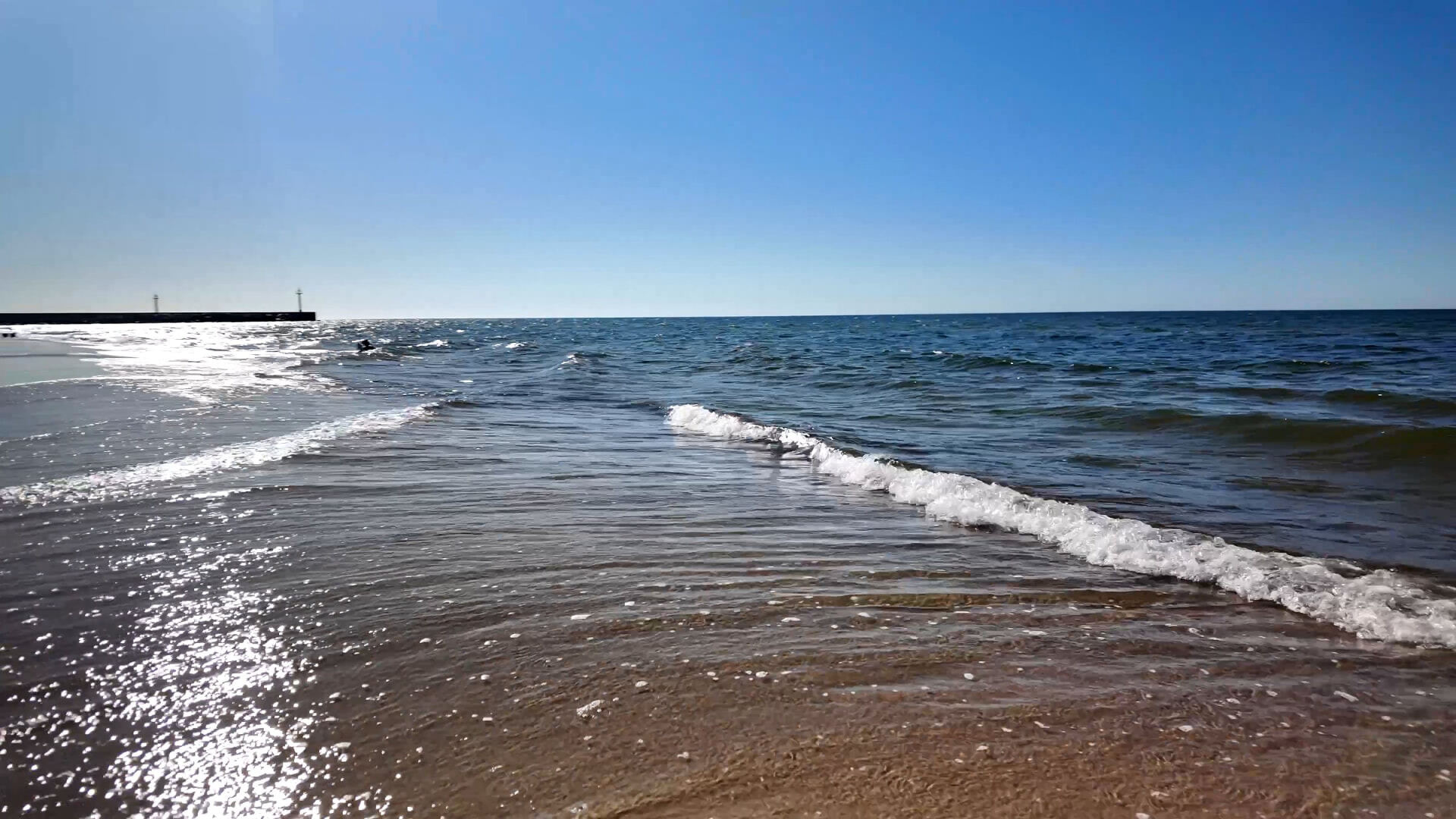 Fala na plaży w Dziwnowie, w tle falochron pod słońce